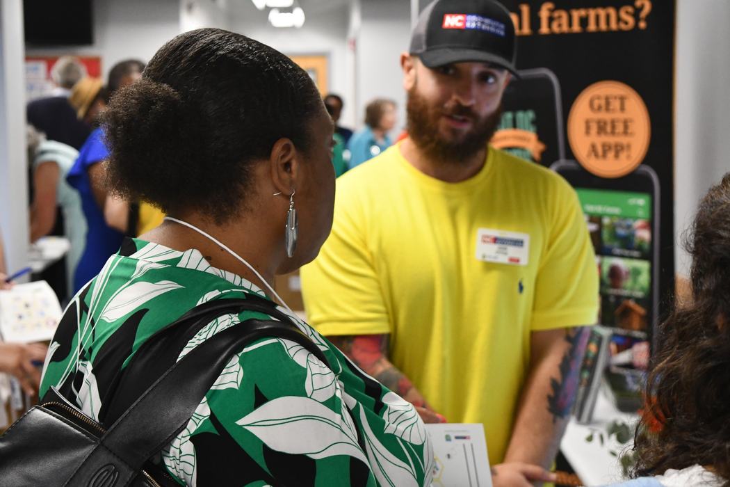 A man in an N.C. Cooperative Extension hat, discusses with a member of the public.