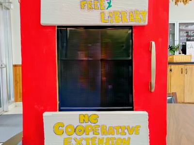Red Little Free Library box with signs "Little Free Library" and "NC Cooperative Extension"