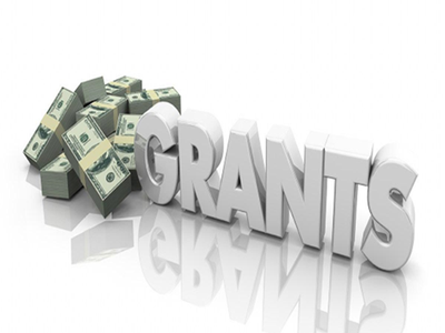 Stacks of US dollar bills next to large 3D word "GRANTS" reflected on white surface