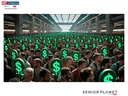 Crowd holding glowing green dollar-sign signs inside a large hall; "Senior Planet" logo
