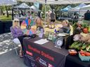 Volunteers sit at a farmers market booth to provide free vegetable donations.