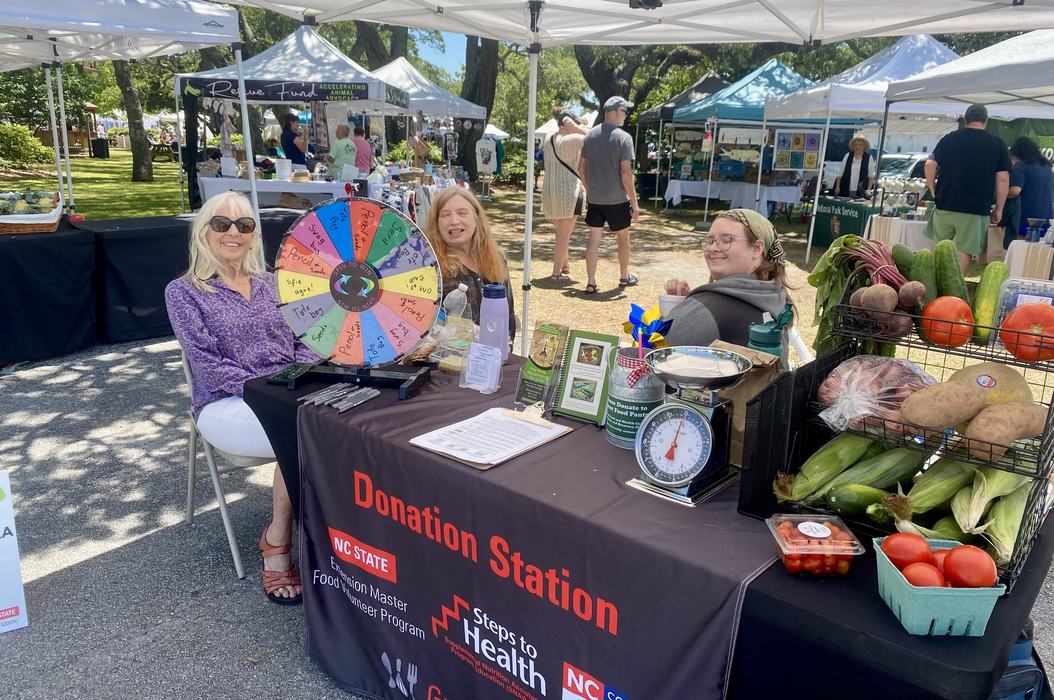 Volunteers sit at a farmers market booth to provide free vegetable donations.