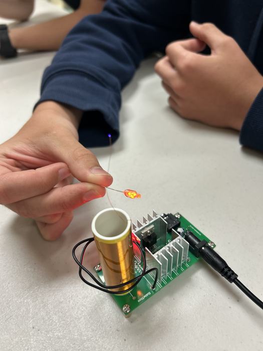 Child demonstrating a mini Tesla coil by holding a small light near it to show how the light activates wirelessly.