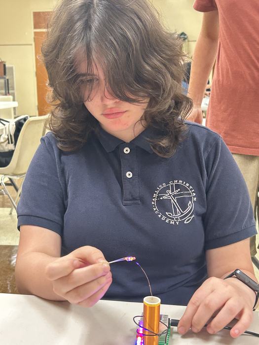 Child testing how a mini Tesla coil can light up a small bulb when a wire is held close to the electromagnetic field.