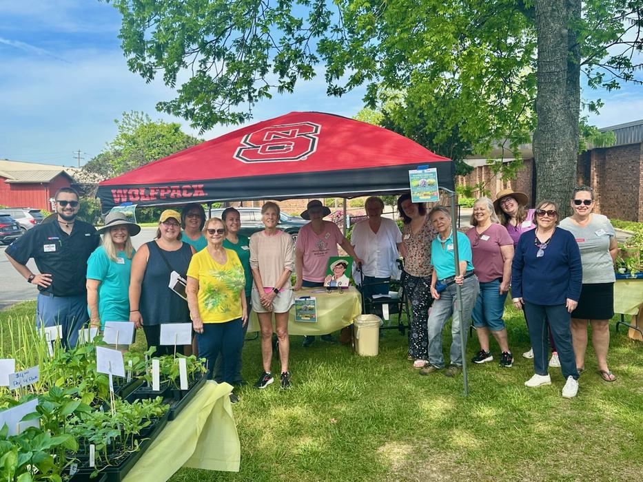 Group of people under red canopy labeled WOLFPACK at outdoor plant sale