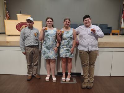 Four students standing on stage holding orange medals