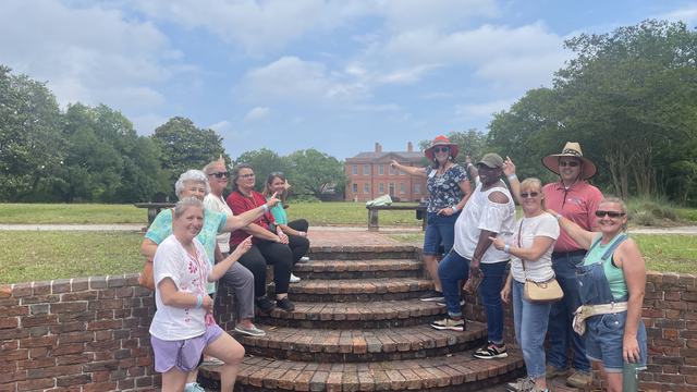 The 2025 Extension Master Gardener class graduates smiling and pointing toward Tryon Palace during a field trip in New Bern, NC.