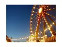 Ferris wheel lit at dusk with illuminated carnival booths and string lights