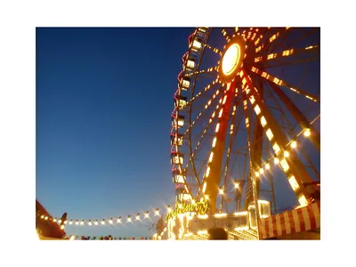 Ferris wheel lit at dusk with illuminated carnival booths and string lights