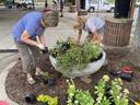 Two women planting flowers in a large concrete planter under a pavilion