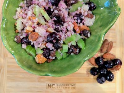 Green bowl of quinoa salad with blueberries, almonds and celery on board labeled "NC Cooperative Extension"