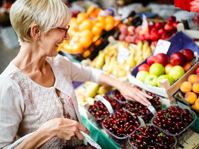 Woman selecting cherries at a market stall with baskets of assorted fruit.