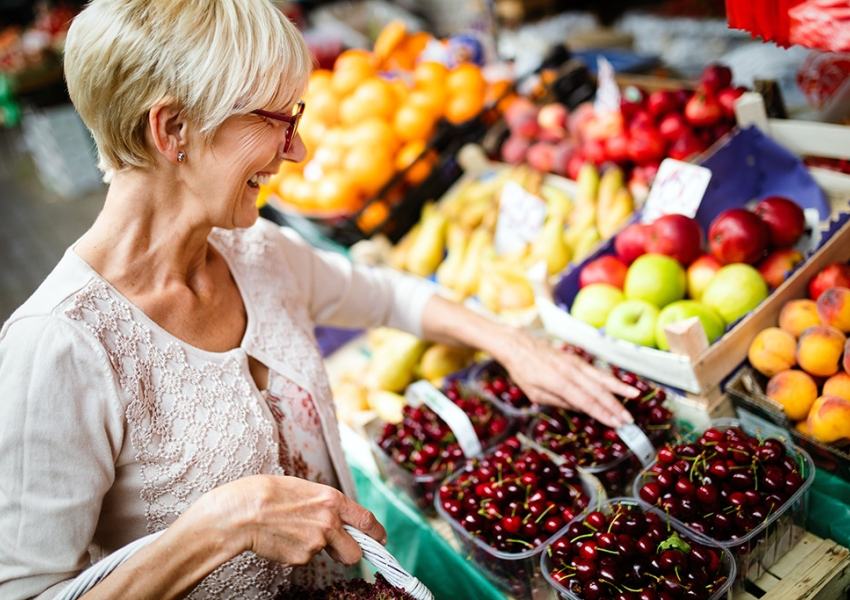 A woman smiles while shopping for a basket of cherries.