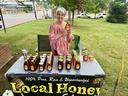 Woman at outdoor table selling jars labeled "Local Honey."