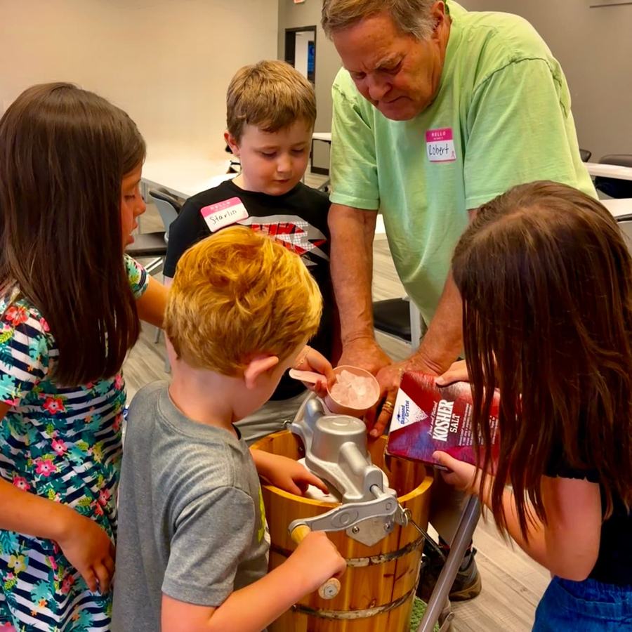 Children pour salt and ice into an icecream hand churn.