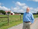 A man in a Cooperative Extension shirt stands on the road to a dairy barn.