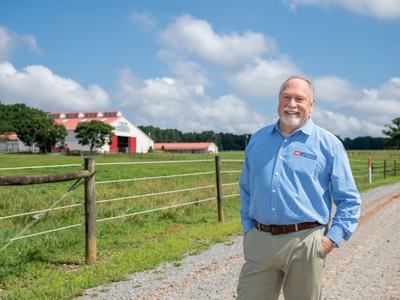 A man in a Cooperative Extension shirt stands on the road to a dairy barn.