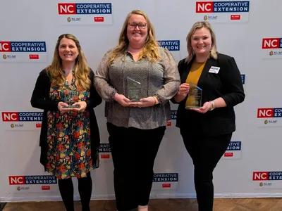 Three women holding awards in front of NC Cooperative Extension backdrop