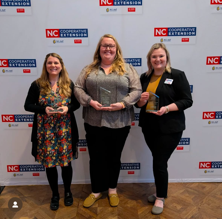 Three women holding awards in front of NC Cooperative Extension backdrop