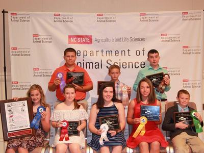 Junior Livestock judges pose in front of the NC State Department of Animal Science banner. They have plaques and ribbons.