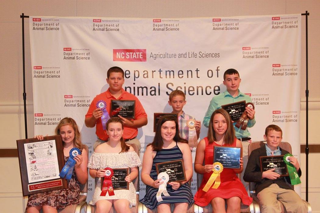 Junior Livestock judges pose in front of the NC State Department of Animal Science banner. They have plaques and ribbons.