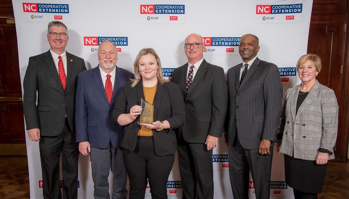 Woman holding award with five people in front of "NC Cooperative Extension" backdrop