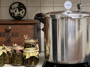Stovetop pressure canner beside jars of pickles and a wooden box labeled "BREAD"