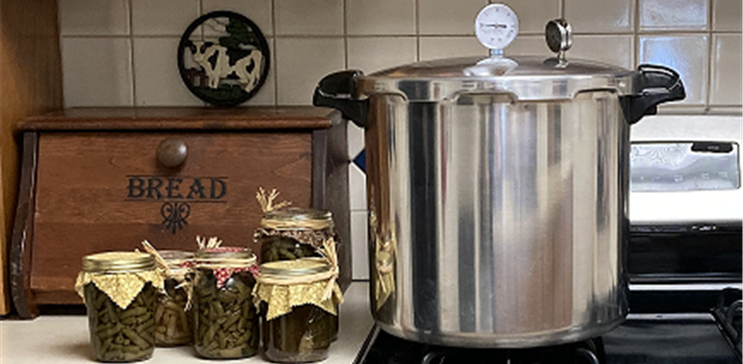 Canned green beans on a counter beside a pressure canner.