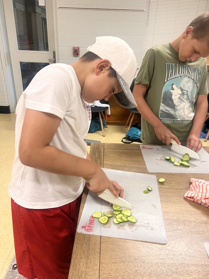 Two boys slicing cucumbers on cutting mats, one mat labeled "EFNEP"