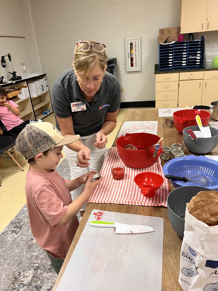 Adult wearing "NC Cooperative Extension" name tag helping child seal a jar at table