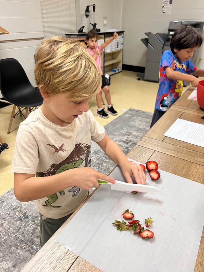 Young child slicing strawberries on a cutting board at a classroom table
