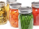 Glass jars of canned vegetables: green beans, sliced carrots, pickles, and tomatoes.