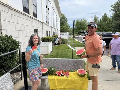 People cutting and holding watermelon slices on a bench outside