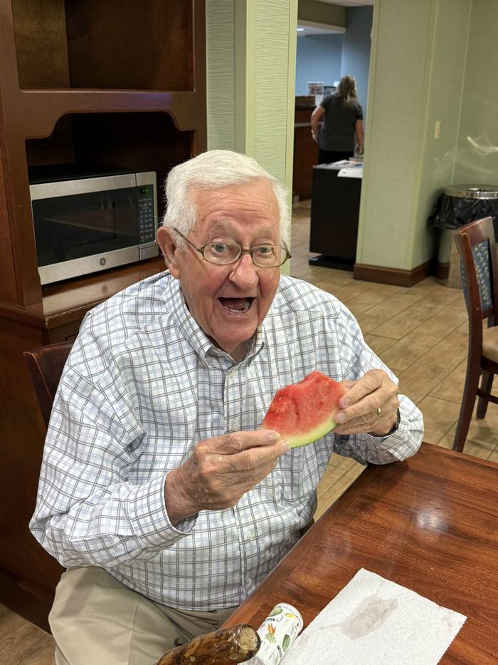 Older man holding and eating a slice of watermelon at a table