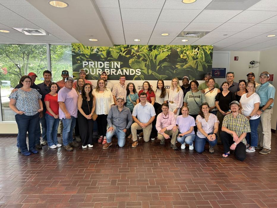 Large group of people posing in front of a wall reading "PRIDE IN OUR BRANDS"