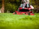 Person on red riding lawn mower cutting grass