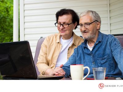 Older couple on porch using a laptop, mug and glass on table; "SENIOR PLANET"