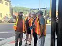 Four people in orange safety vests on a street corner, one man pointing and directing