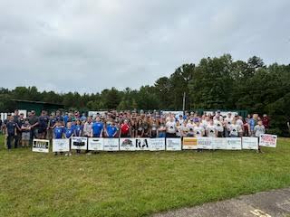 Groups of 4-H Young Guns Competitors pose together with sponsor signage.