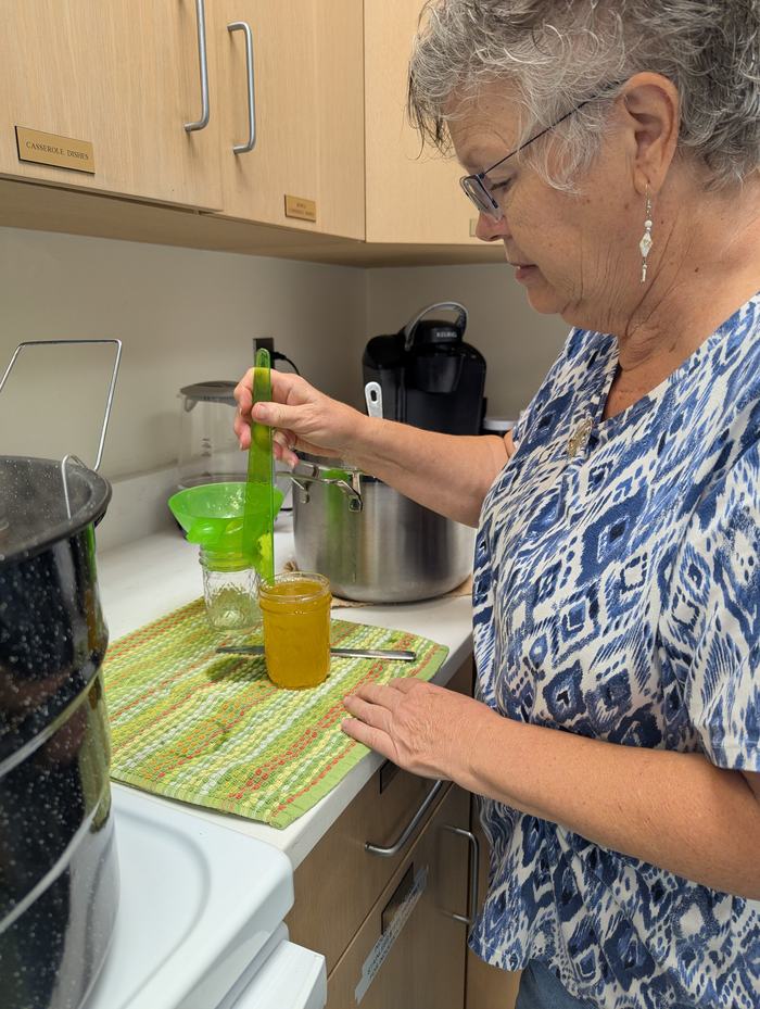 A woman fills a jar to be canned.