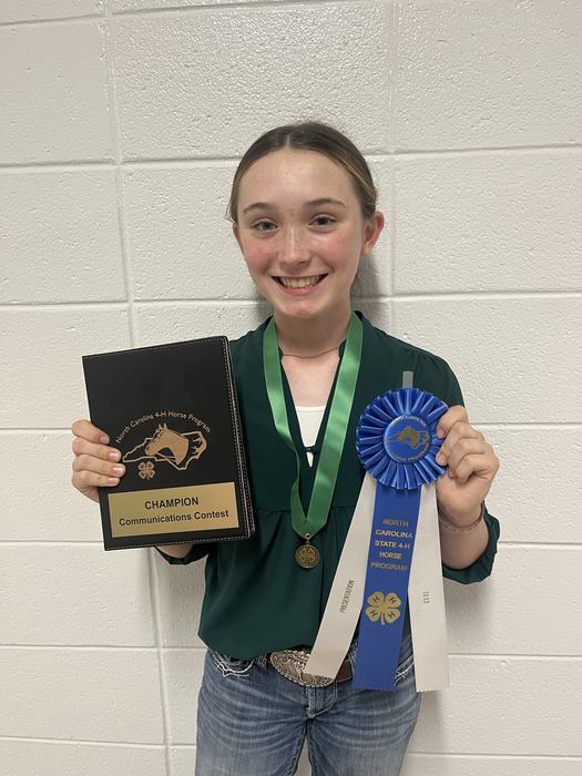 Person holding plaque "CHAMPION Communications Contest" and ribbon "NC 4‑H Horse Program"