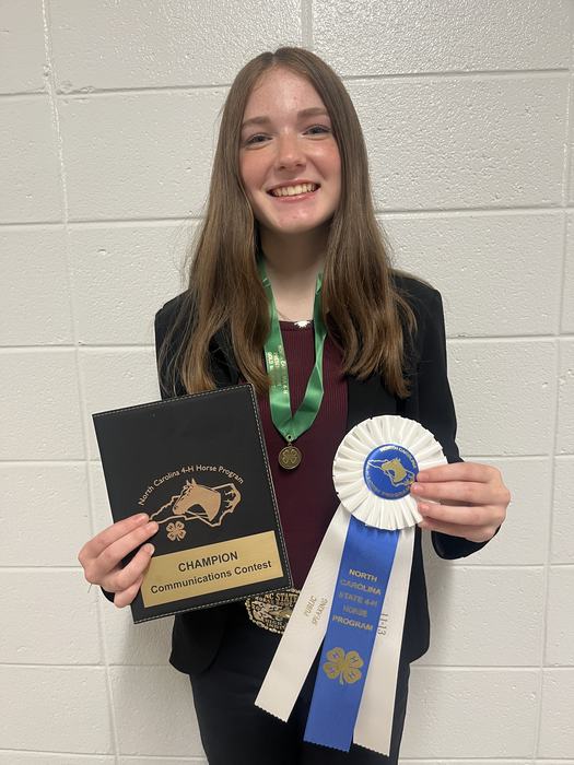Teen holding "CHAMPION Communications Contest" plaque and North Carolina 4-H blue ribbon