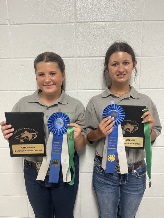 Two students holding "CHAMPION Communications Contest" plaques and blue ribbons