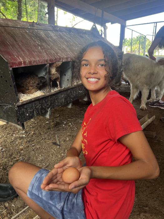 Girl in Red shirt holding egg that she just gathered from chickens