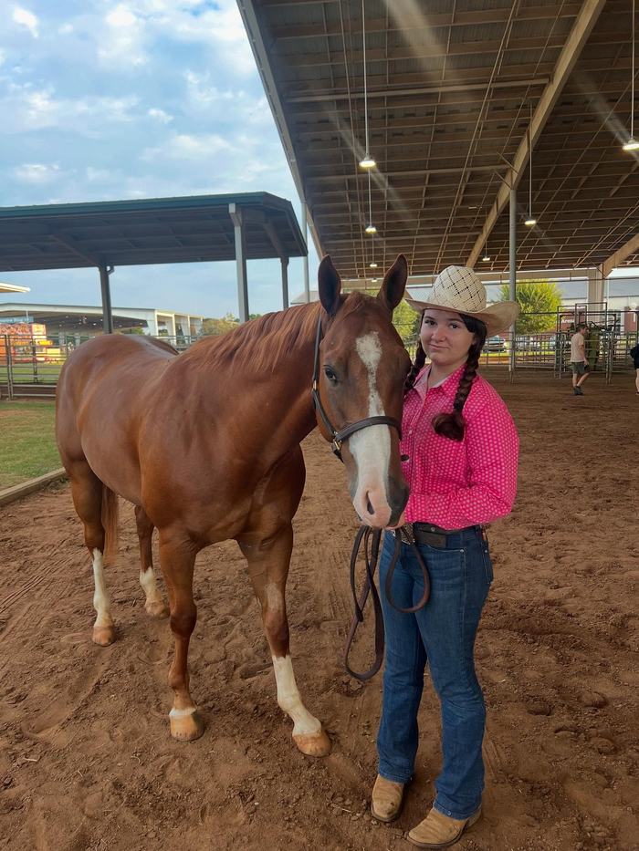 Young woman in cowboy hat holding reins of a chestnut horse in a covered arena
