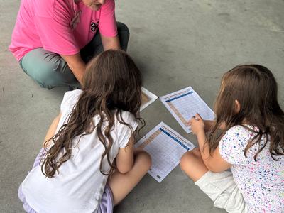 A woman helps two young girls fill out a worksheet.