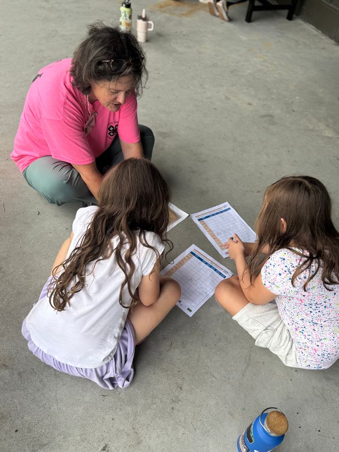 A woman helps two young girls fill out a worksheet.