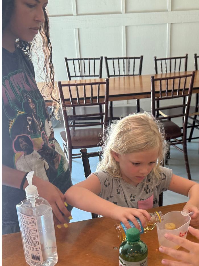 A girl pours a liquid from a bottle into a measuring cup.