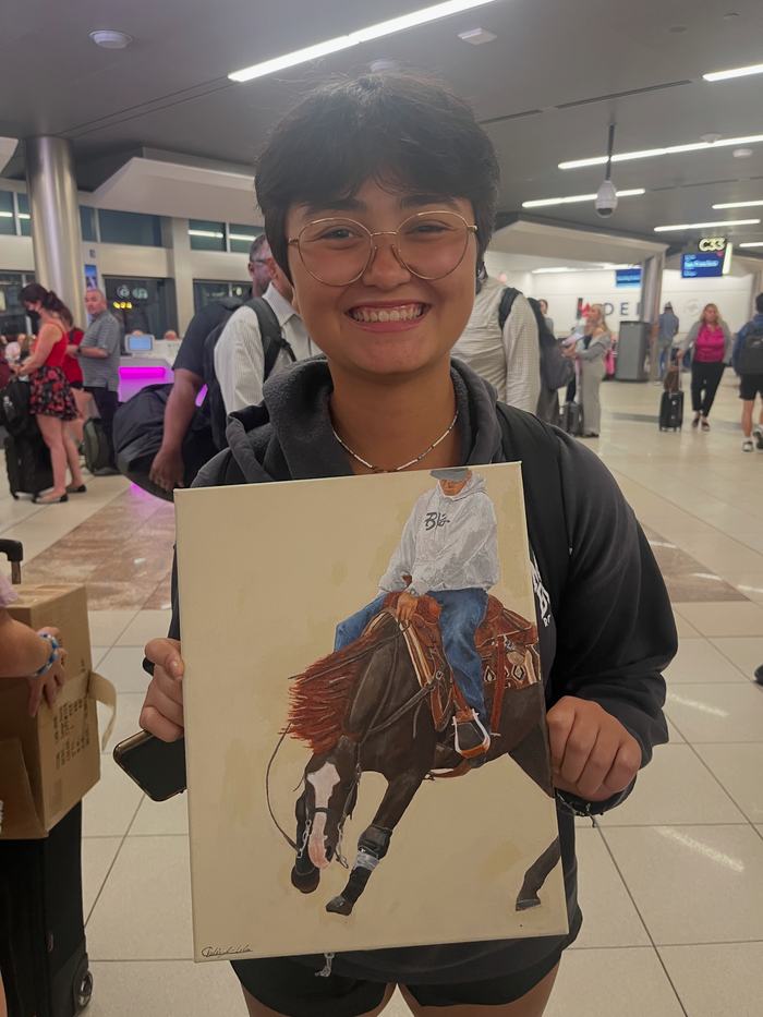 Person with glasses holding painting of a rider on a horse in an airport terminal