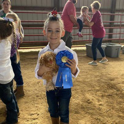 A girl poses with her chicken and a blue ribbon.